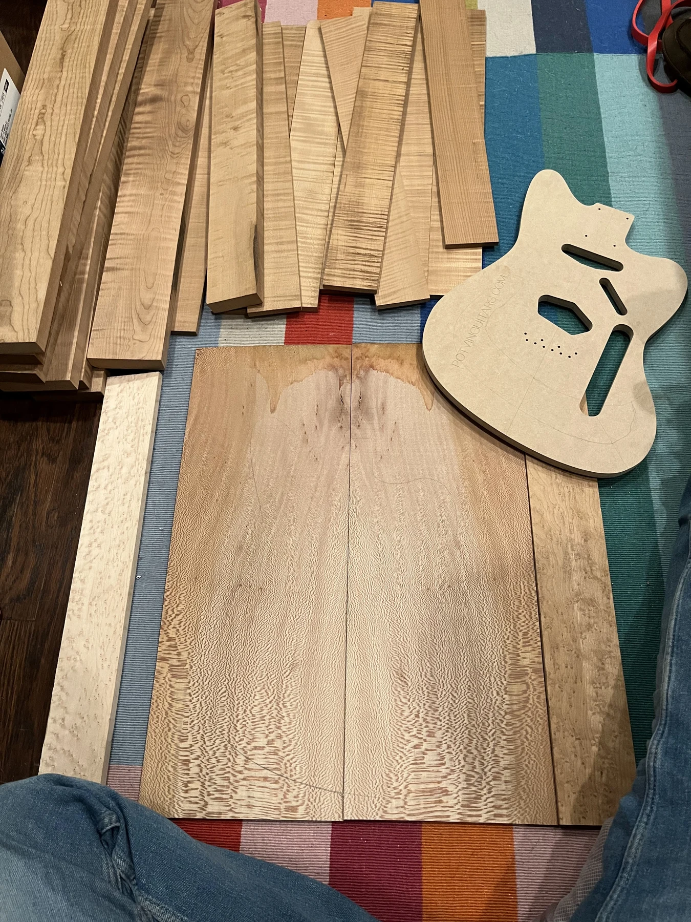 Figured wood stock, neck blanks, and a routed guitar body arranged on a work surface